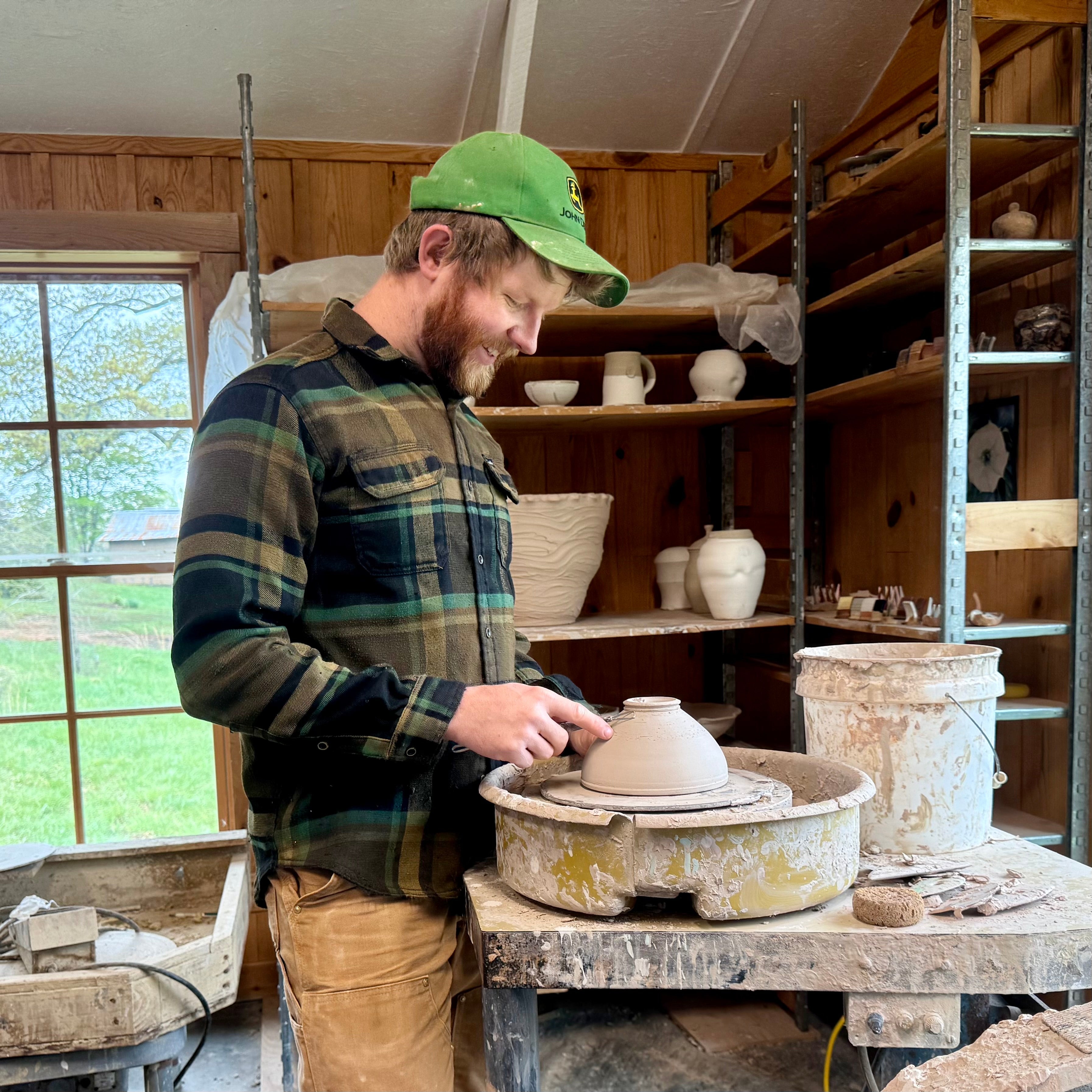 Sam Dougherty at wheel trimming an upside down ceramic bowl in Stokes County pottery studio.