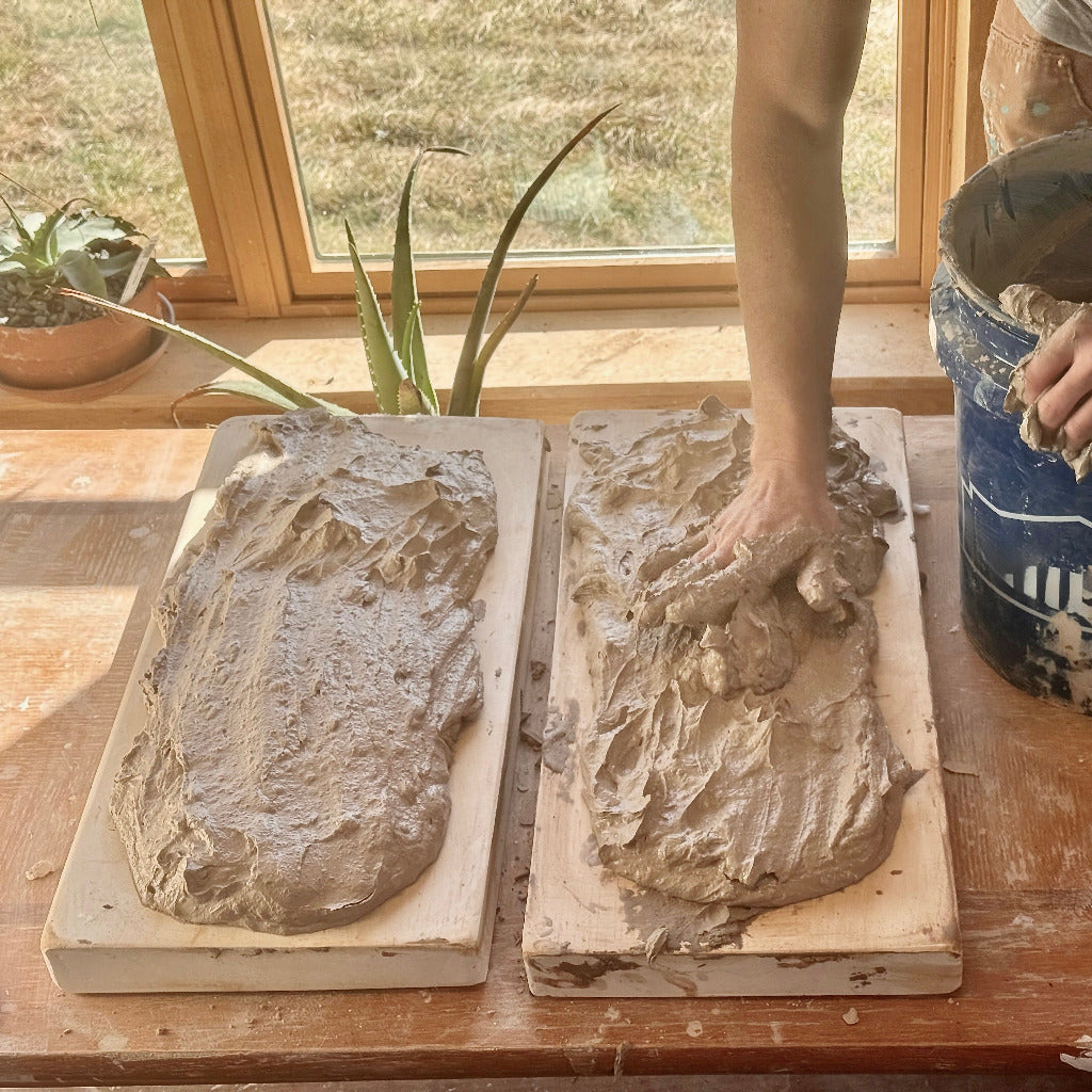 Two plaster boards with an artists arm putting slurry (clay) onto the boards to de-water it.