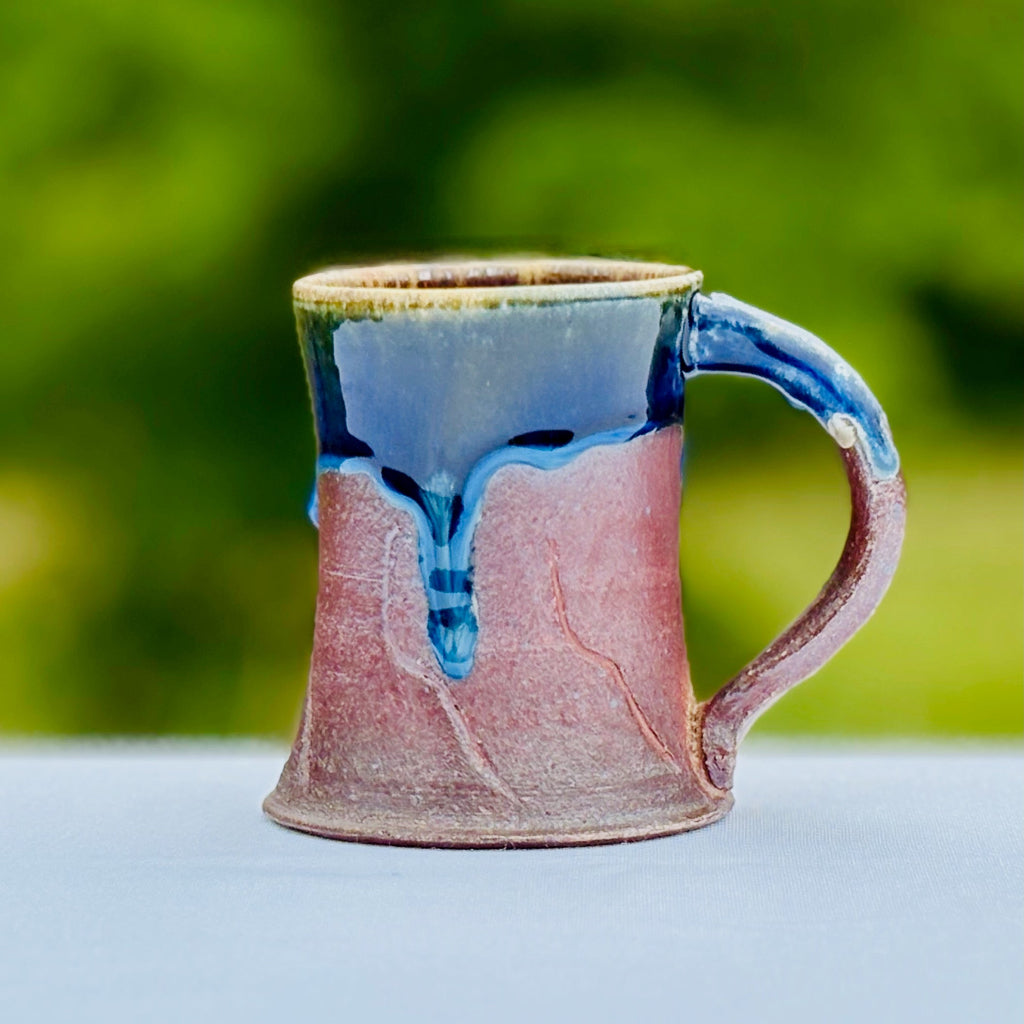 ceramic mug with cobalt runs over unglazed base on a blurred green background