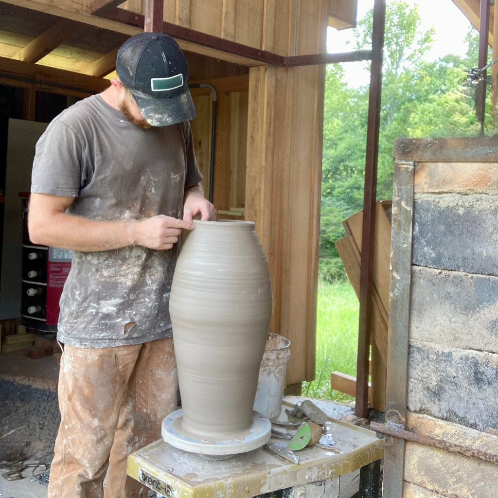 Sam Trimming a large pottery on wheel outside by the wood-fired kiln.