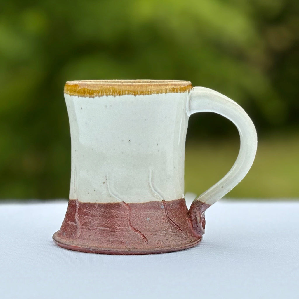 Pottery mug with a gold rim which contrasts with the glossy white glaze and rich brown base