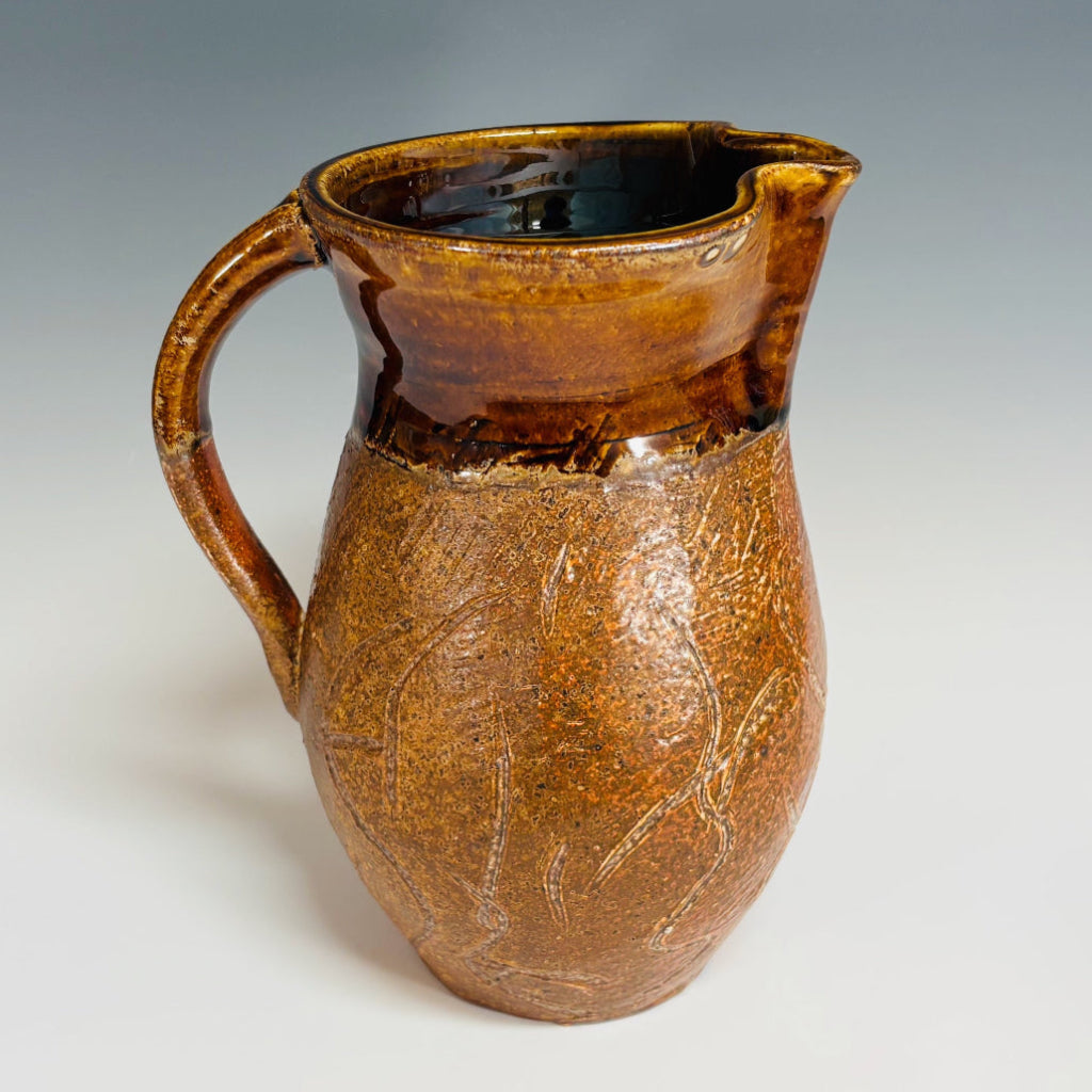 Side view of hand-thrown stoneware pitcher showing textured surface and natural wood-firing effects.