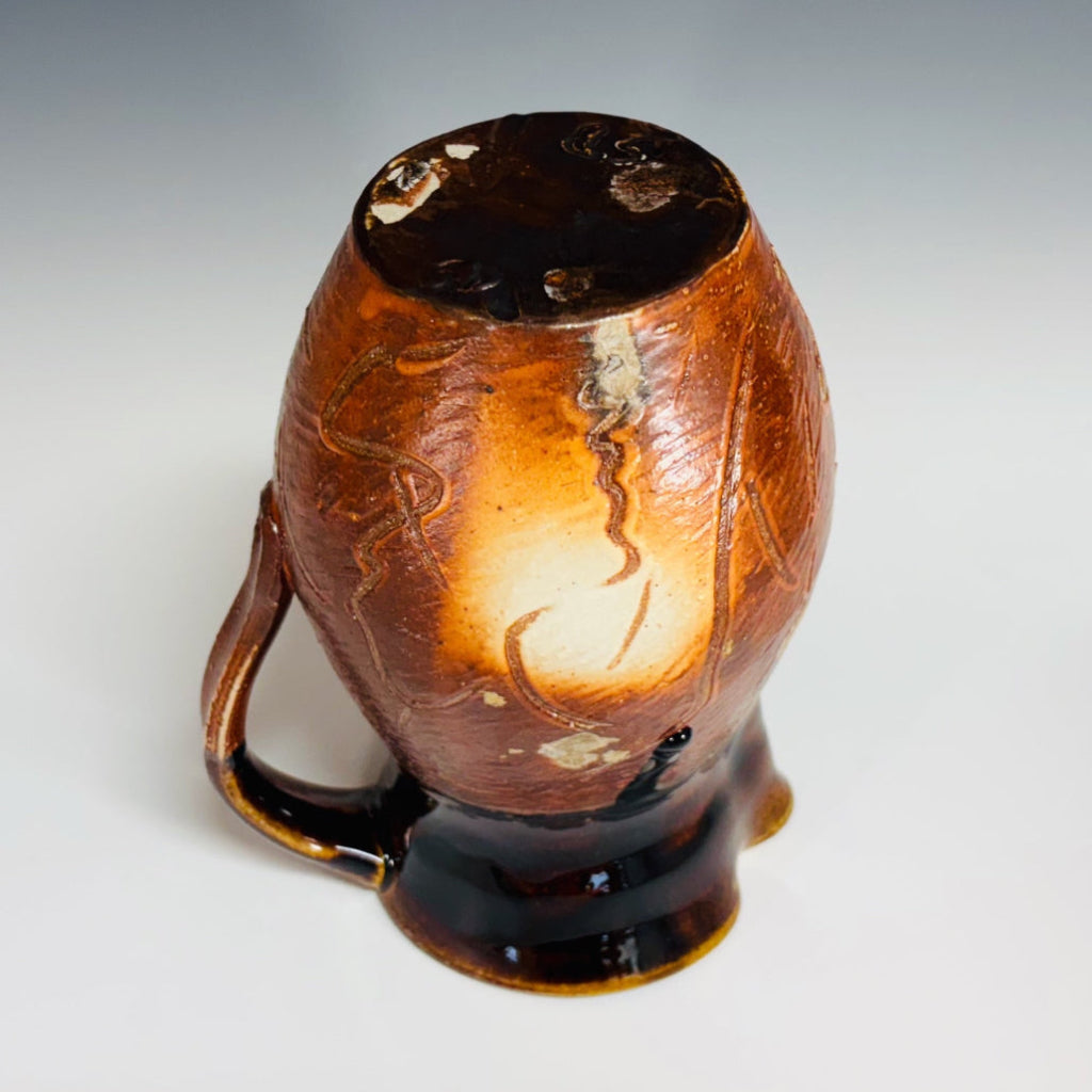 Bottom view: Handcrafted amber and chocolate brown wood-fired stoneware pitcher with pouring spout and handle.