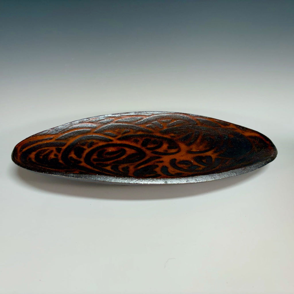 Decorative oval serving tray with delicate brown-black swirls over an orange flashing base. 