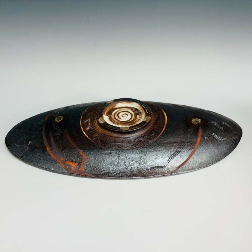 Bottom view: Decorative oval serving tray with delicate brown-black swirls over an orange flashing base with a little circular base. 