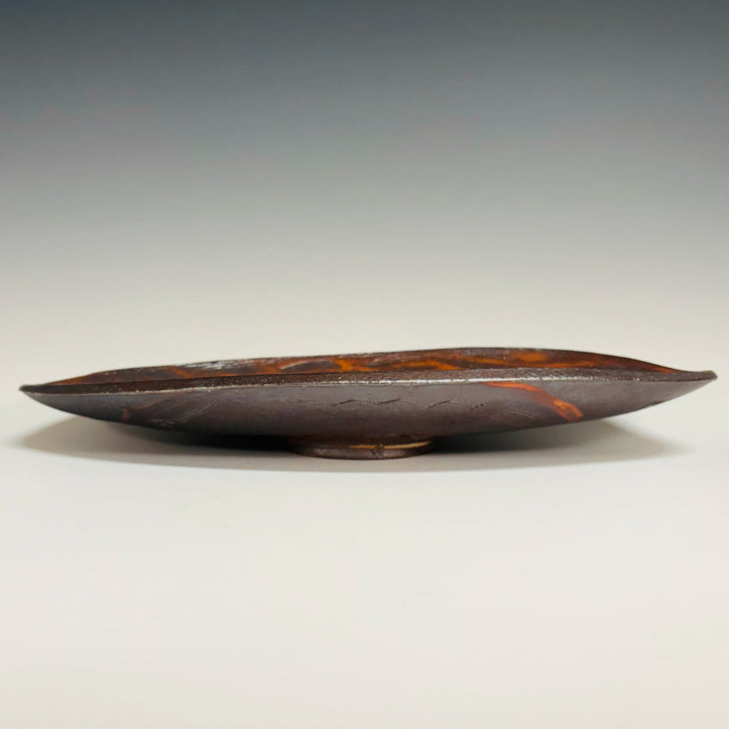 Side view: Decorative oval serving tray with delicate brown-black swirls over an orange flashing base with a little base.