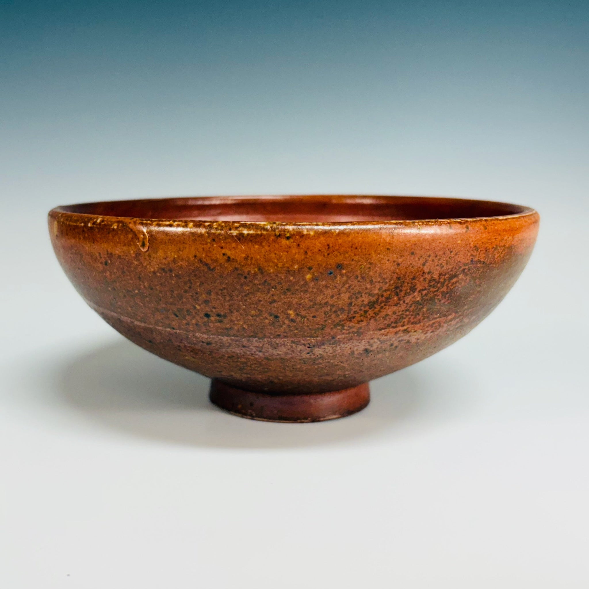 Orange pottery bowl with dark brown speckles, delicate base, large white dot inside bowl. 