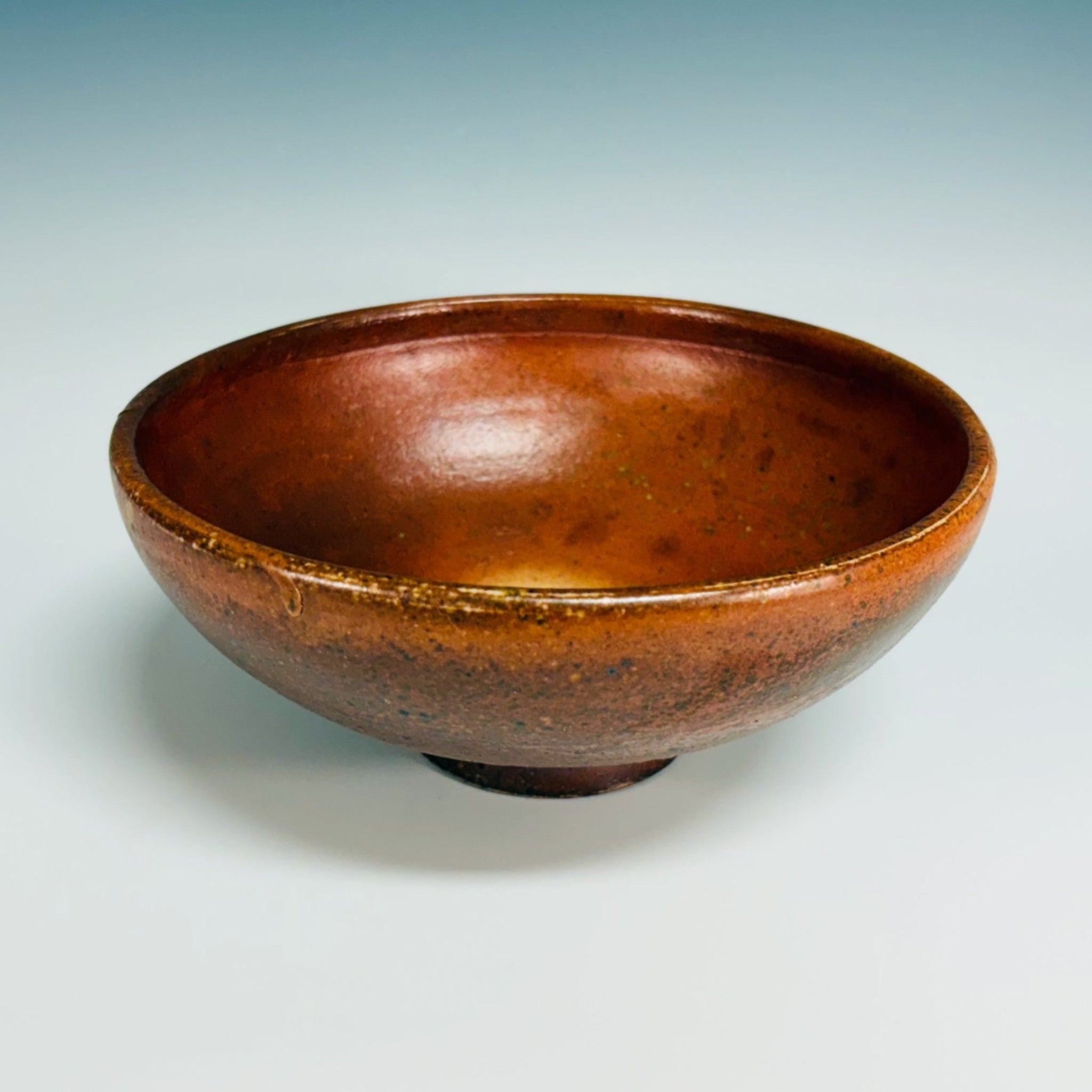 Orange pottery bowl with dark brown speckles, delicate base, large white dot inside bowl. 