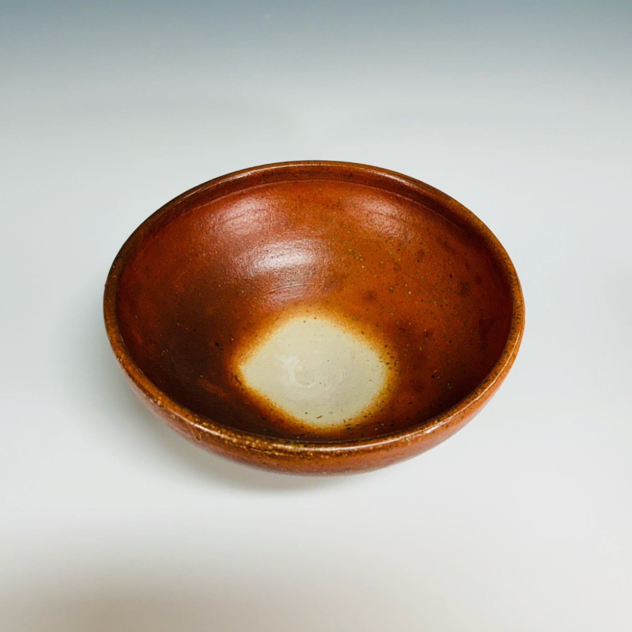 Orange pottery bowl with dark brown speckles, delicate base, large white dot inside bowl. 