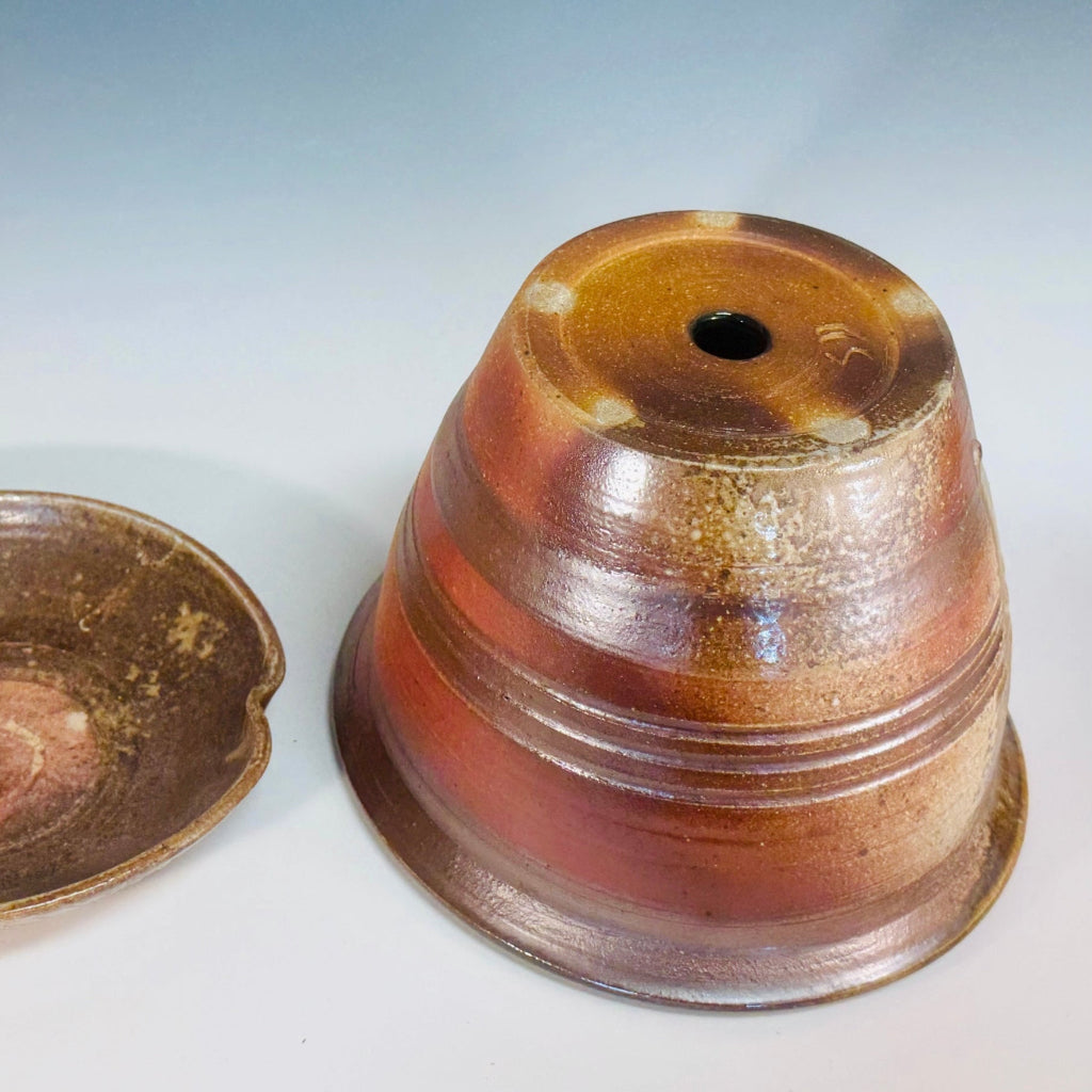 Handcrafted wood-fired ceramic planter with copper and bronze glaze, featuring textured horizontal lines and matching saucer