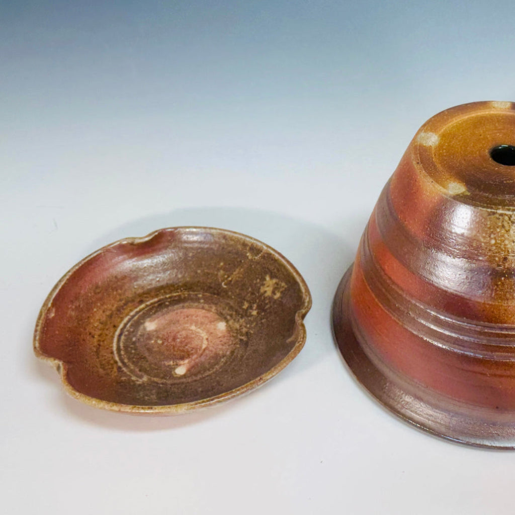 Handcrafted wood-fired ceramic planter with copper and bronze glaze, featuring textured horizontal lines and matching saucer