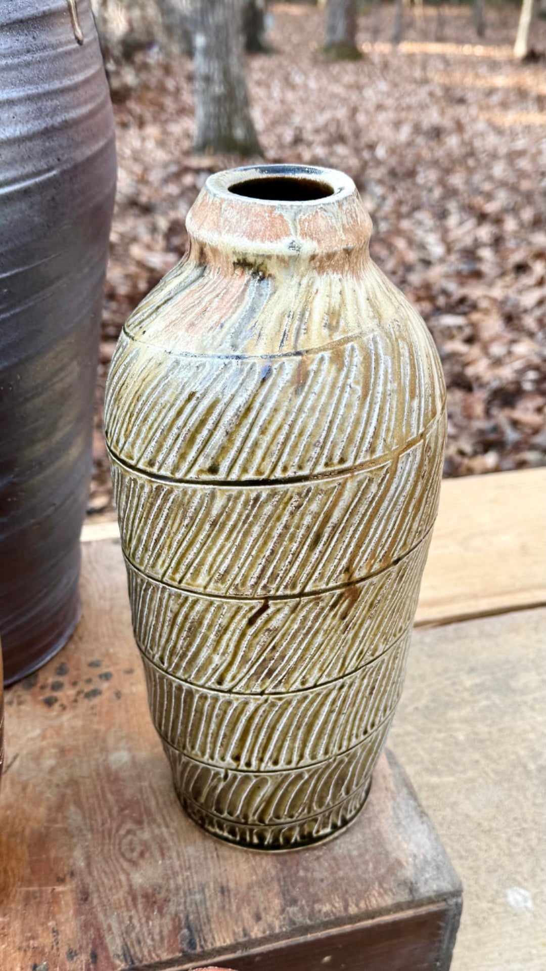 Hand-thrown large pottery vase with diagonal lines and horizontal lines, dark brown interior and white, blush pink, black and beige exterior on a wooded riser.