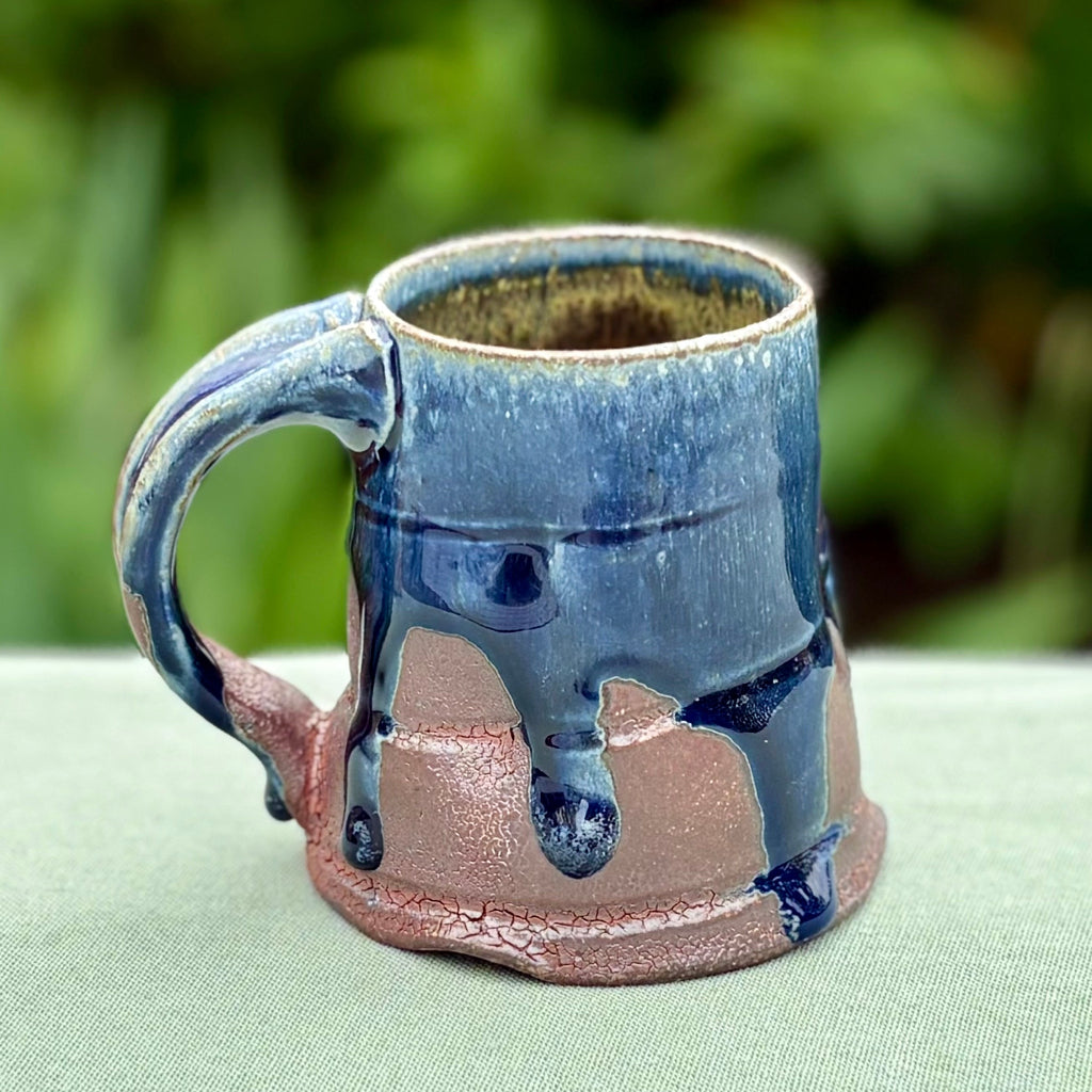 A ceramic mug with a deep blue cobalt glaze and earthy red brown shino color, featuring incised and dimpled decoration