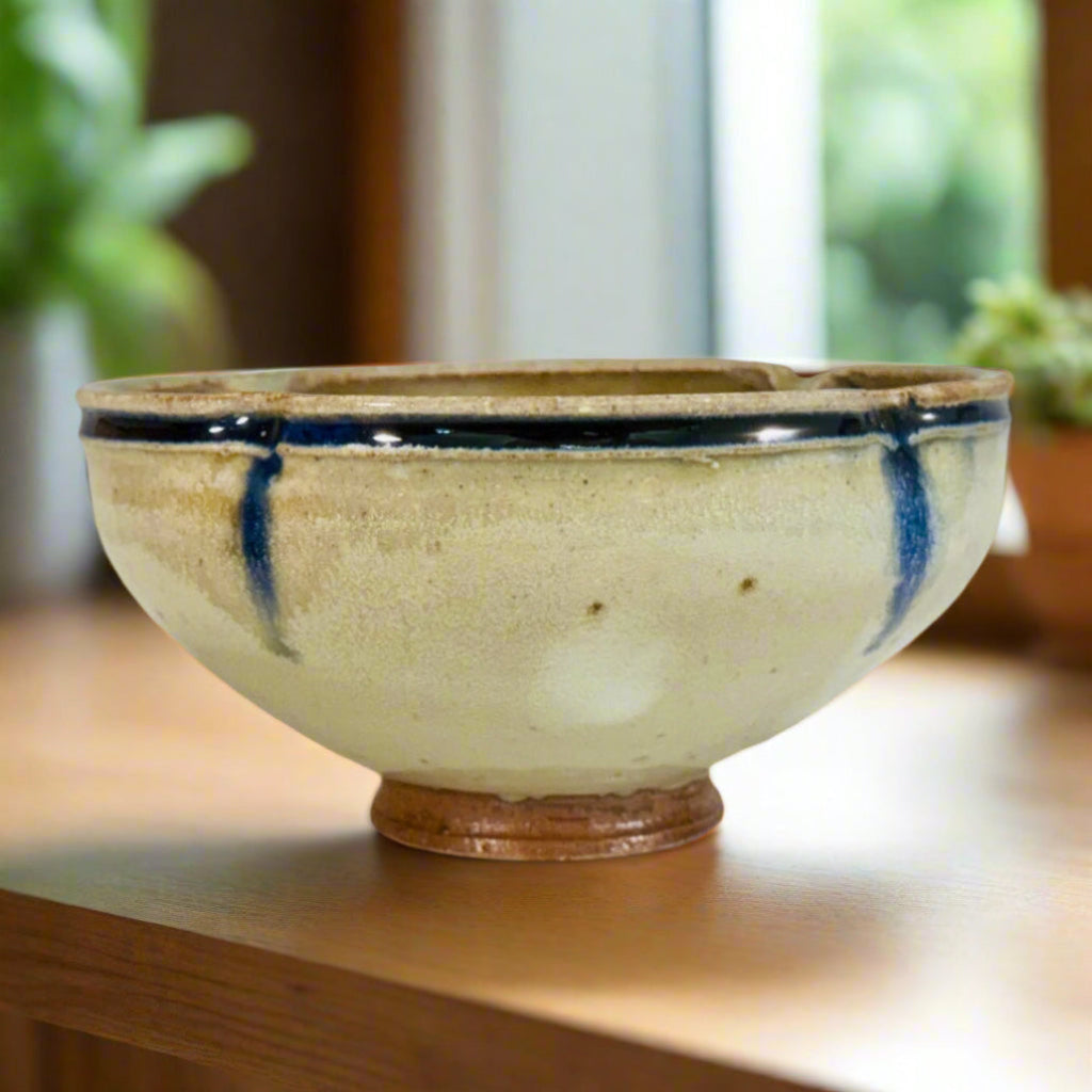 Handcrafted wood-fired ceramic bowl with cream body, cobalt blue vertical streaks, and earthy brown foot, made by artisans in Danbury, NC.
