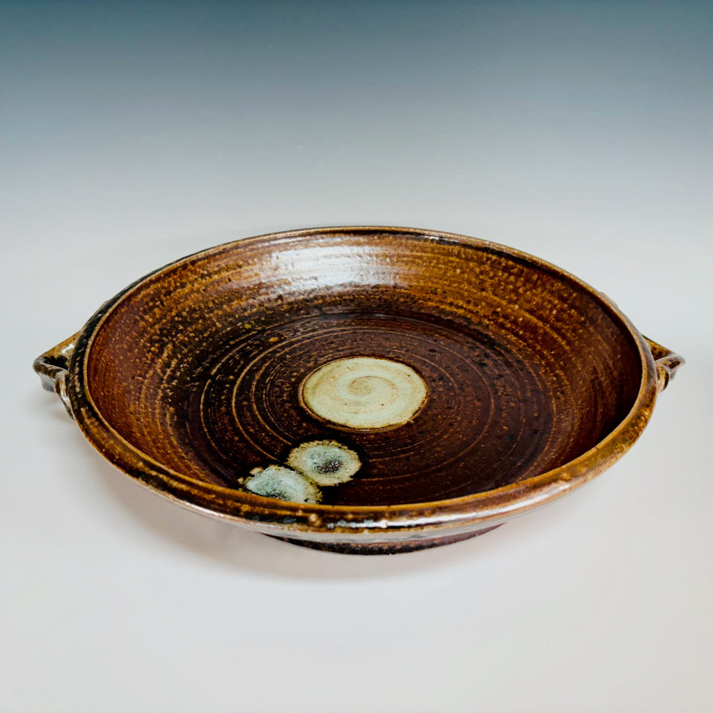 Handcrafted brown ceramic serving platter with integrated handles, concentric rings and cream spiral medallion center.