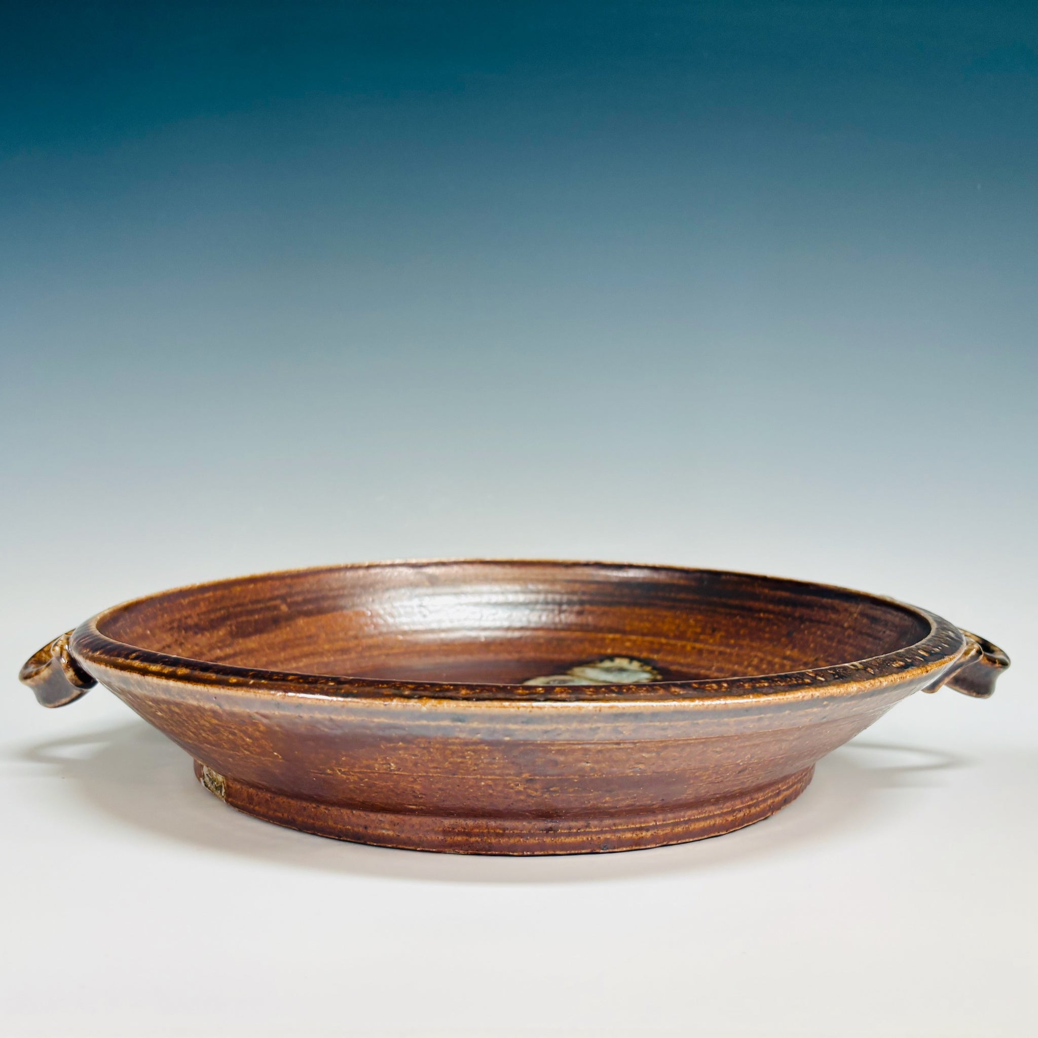 Side view Handcrafted brown ceramic serving platter with integrated handles, concentric rings and cream spiral medallion center