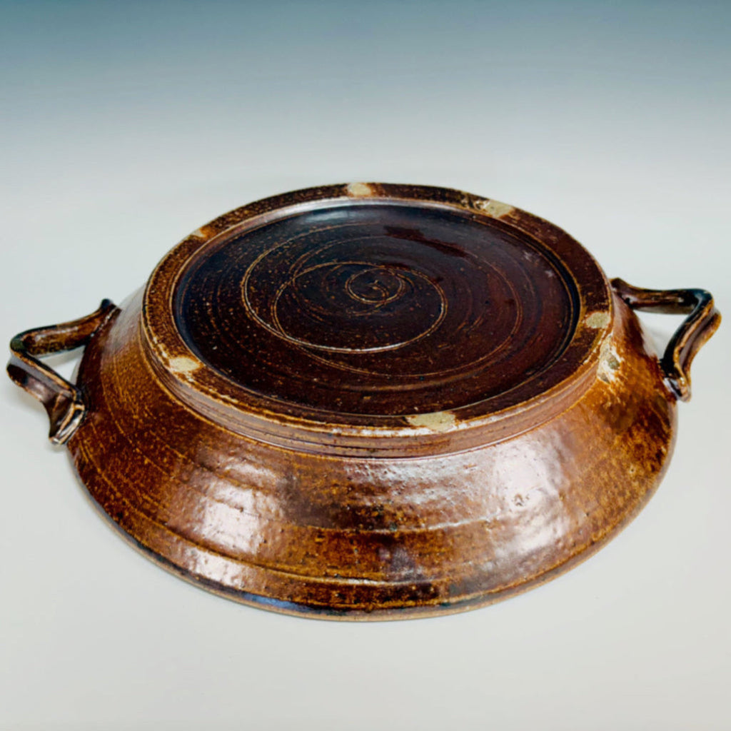 Bottom view:  Handcrafted brown ceramic serving platter with integrated handles, swirls and dots on the bottom.