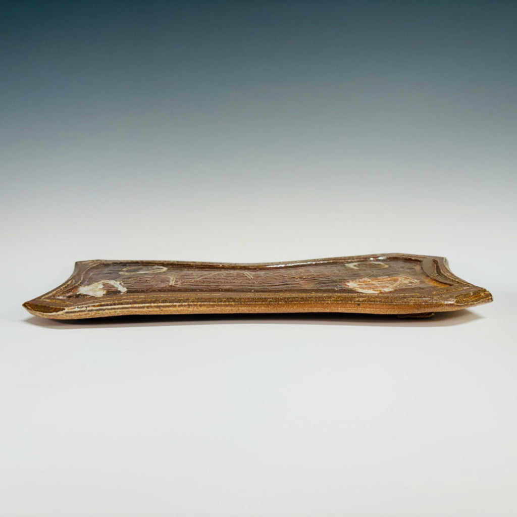 Handmade curved rectangular serving tray with white decorative accents on rich auburn surface, wood-fired in North Carolina.