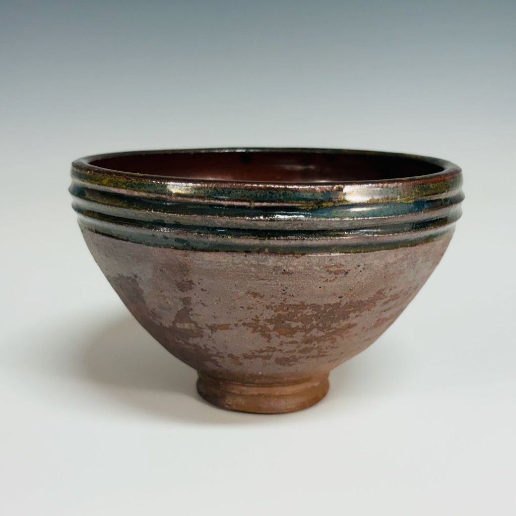 Pottery bowl with a green rim with three groves, brown interior and exterior and a delicate base.