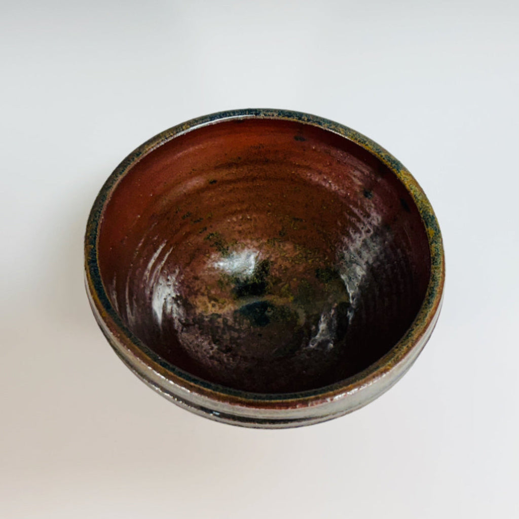 Pottery bowl with a green rim with three groves, brown interior and exterior and a delicate base.