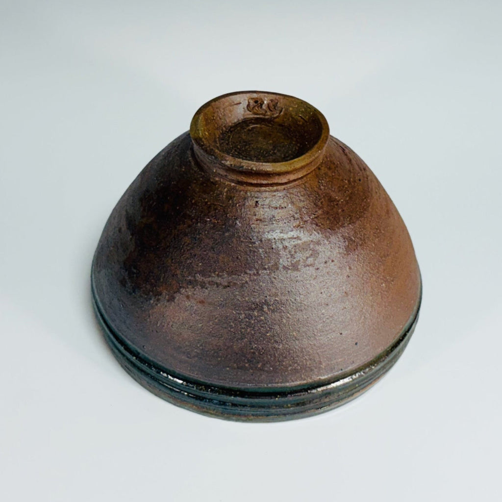Pottery bowl with a green rim with three groves, brown interior and exterior and a delicate base.