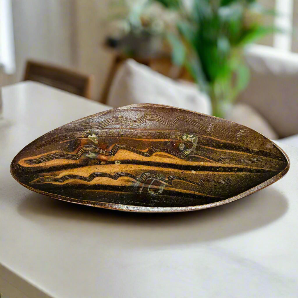 Handmade elongated oval serving tray with natural wave patterns in earthy brown tones on a kitchen counter, wood-fired in North Carolina.