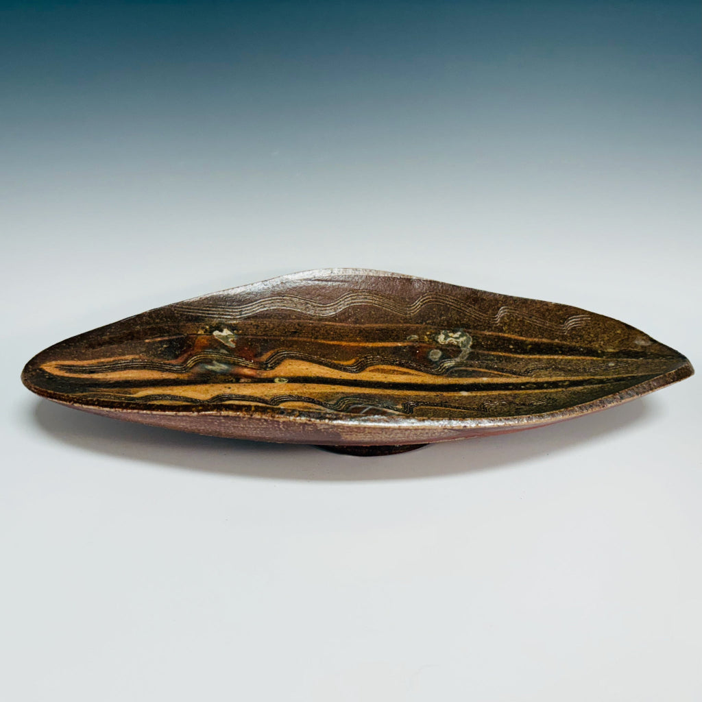 Handmade elongated oval serving tray with natural wave patterns in earthy brown tones, wood-fired in North Carolina.
