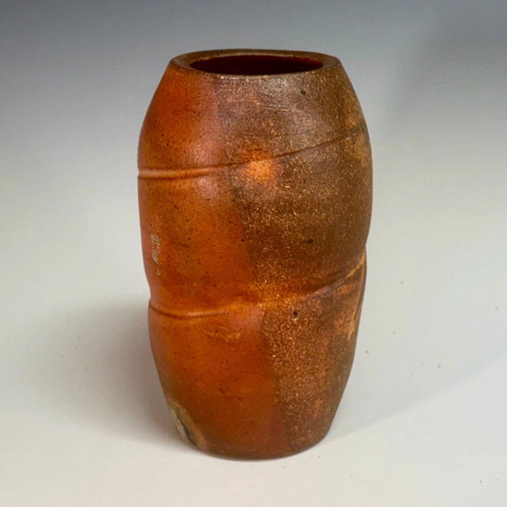 Handcrafted wood-fired ceramic vase in vibrant orange with natural ash deposits and horizontal banding.
