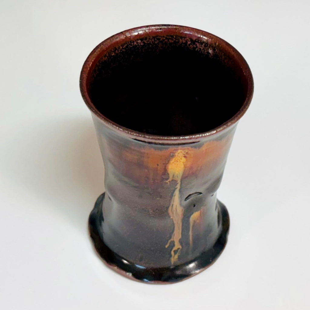 This cup is a handcrafted wood-fired cup with dark brown/black glaze with amber drip from rim to base and speckled rim.