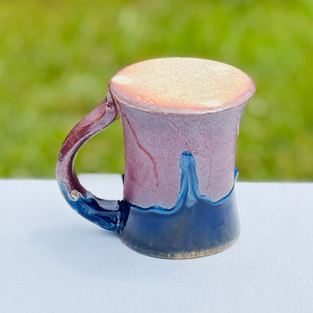 Ceramic coffee mug with unglazed bottom with three light dots, artist's mark, and cobalt glaze drips over a bright amber brown body