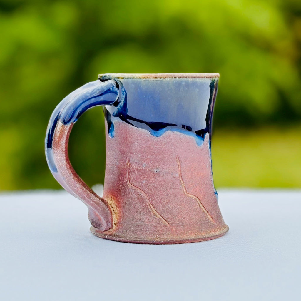 handmade ceramic coffee mug triking cobalt glaze drips over a bright amber brown base and abstract line decoration