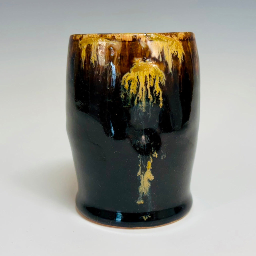 Handcrafted black stoneware tumbler with golden amber drip glaze from wood-fired kiln.