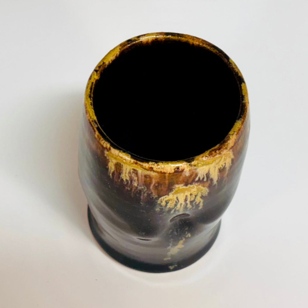 Handcrafted black stoneware tumbler with golden amber drip glaze from wood-fired kiln