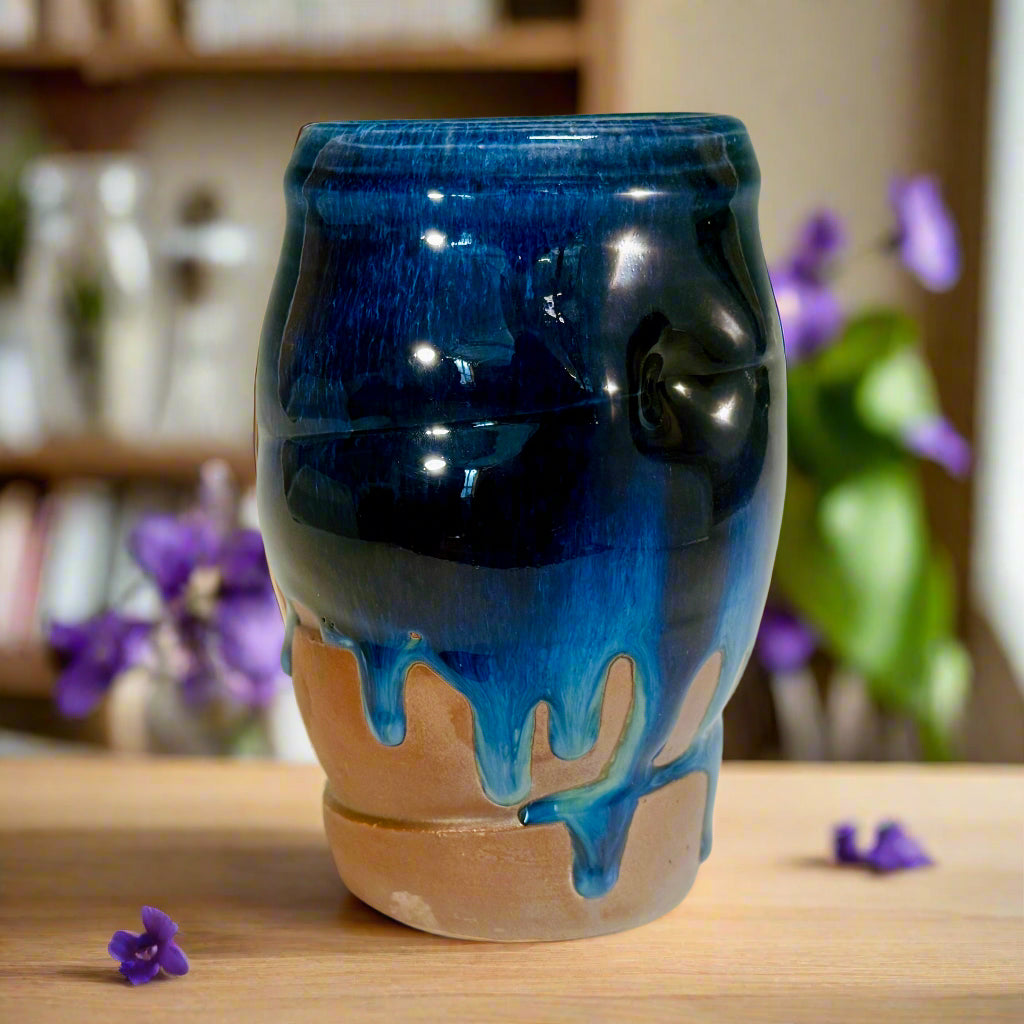  Artisan medium vase with deep blue glaze flowing over orange flashing slip with flowers around base and in background. 