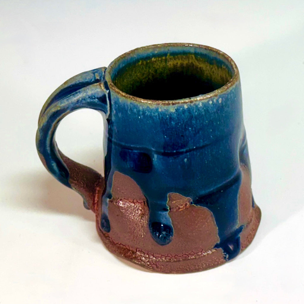 Handcrafted wood-fired ceramic mug with dramatic midnight blue glaze dripping over earthy clay body and sturdy handle.