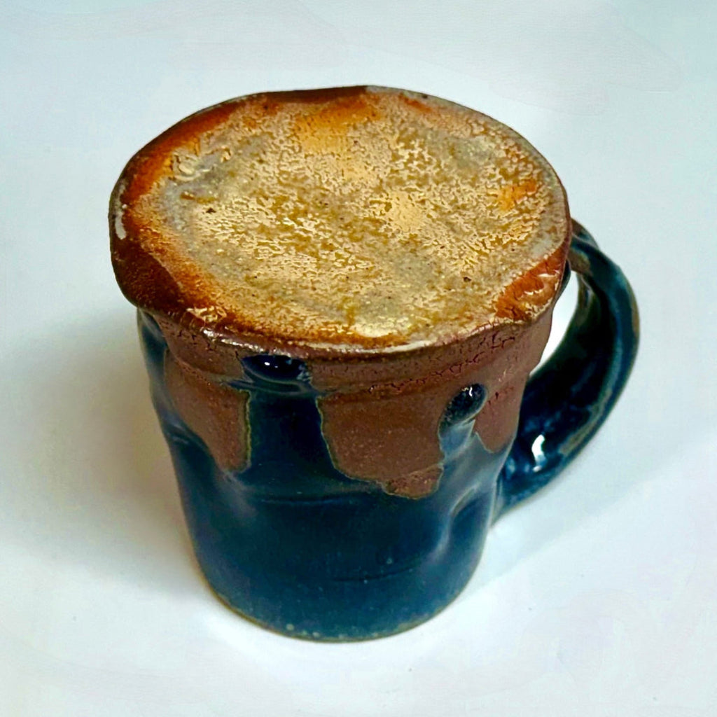 Handcrafted wood-fired ceramic mug with dramatic midnight blue glaze dripping over earthy clay body and sturdy handle. Bottom of cup.