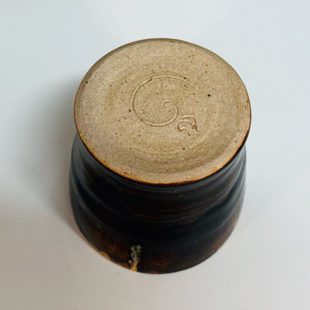 dark brown wood-fired pottery cup with natural amber drip glaze, handcrafted texture, and a cream color bottom.
