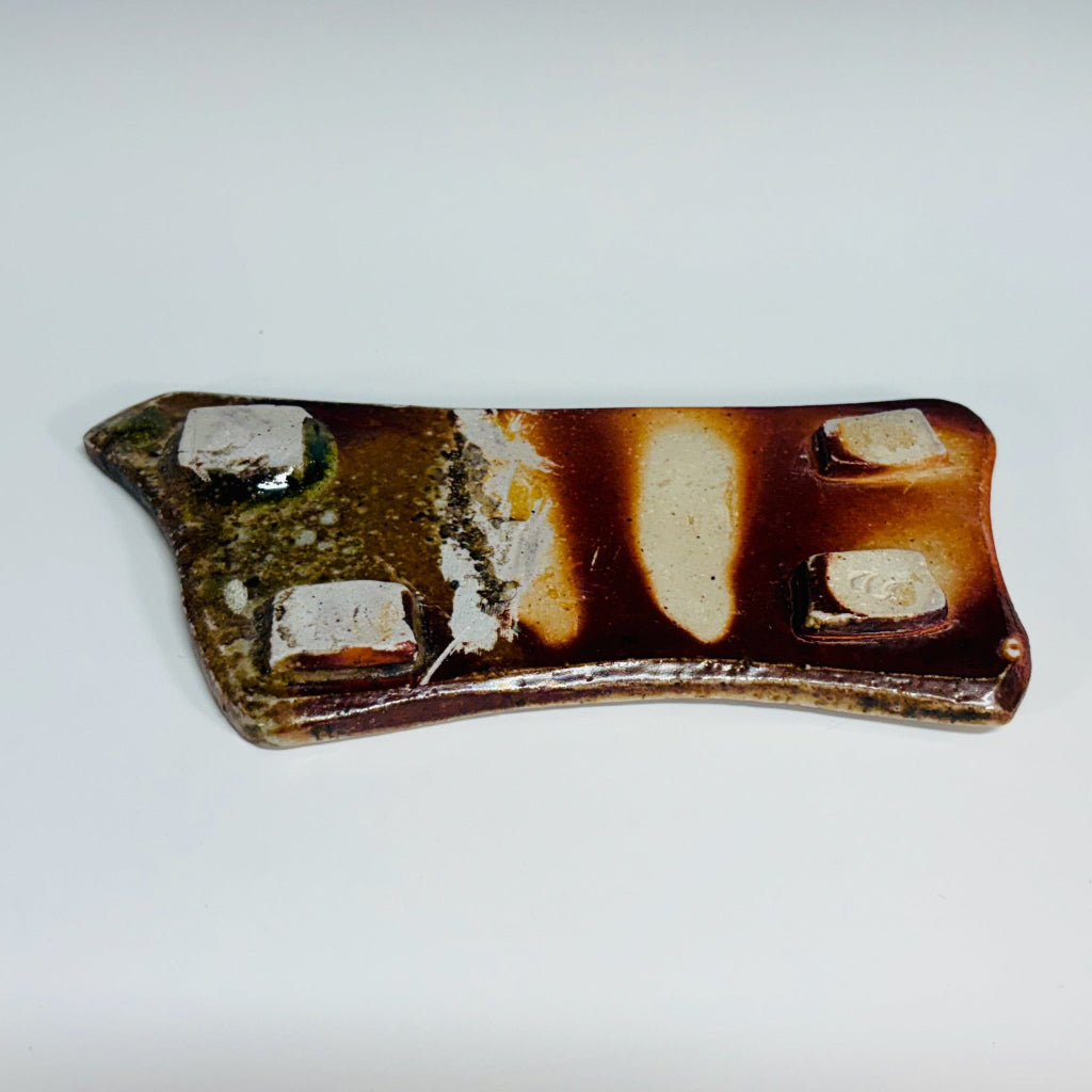 Underside of soap dish. 4 square white feet and varied colors of amber, cream, green and a mix between shiny and matte.