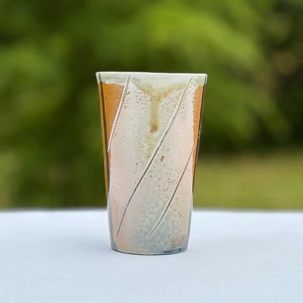 Side profile of striped wood-fired porcelain cup showing gradient color variation and artisan craftsmanship.
