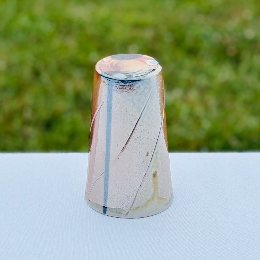 Bottom view of handmade wood-fired porcelain cup by Sam Dougherty showing unglazed base dots of white and black glazing.