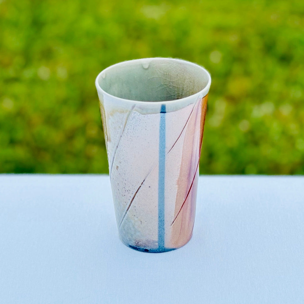 Side profile of porcelain cup with a peek of the interior celadon gaze and a striped wood-fired showing gradient color variation and artisan craftsmanship. 