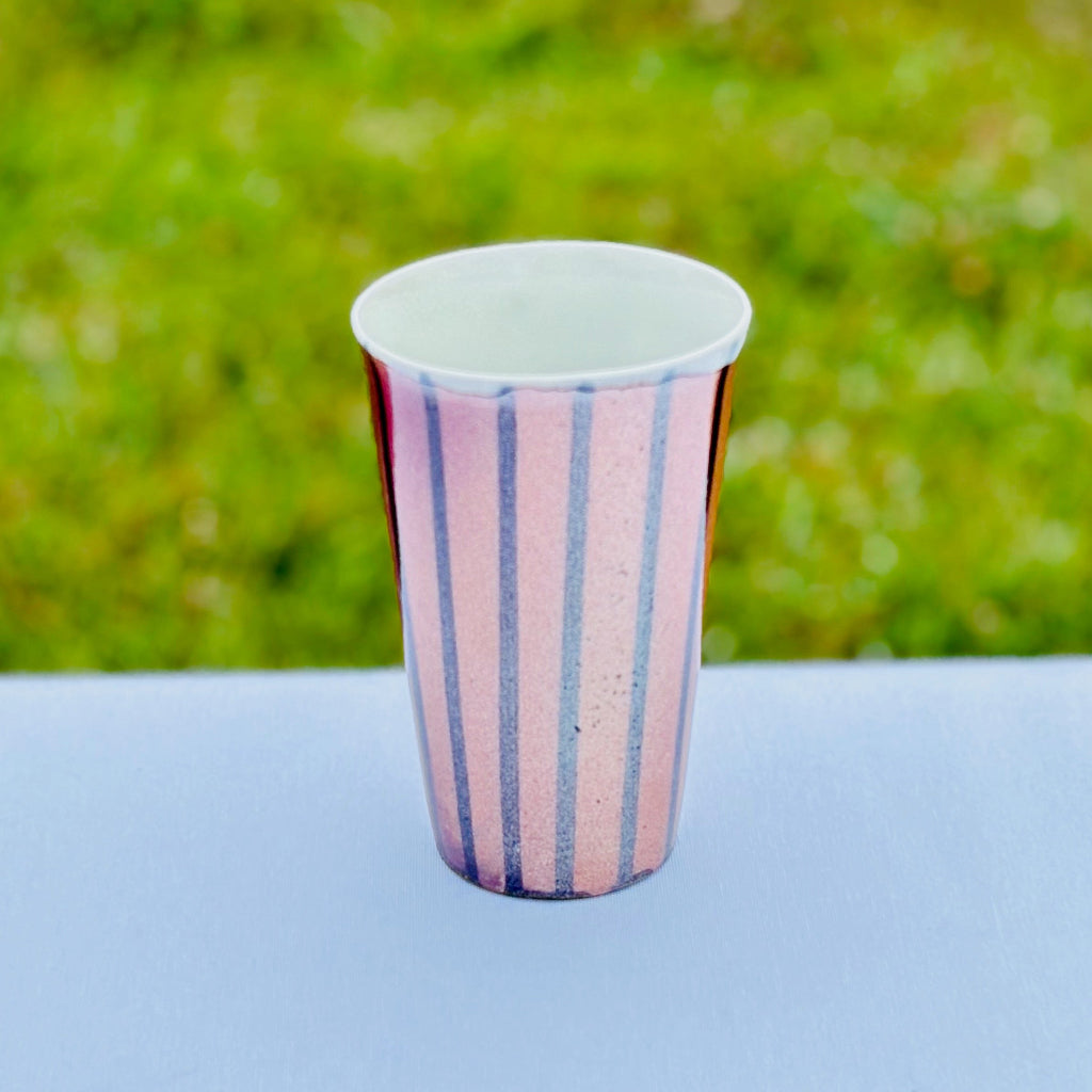 Top View: Porcelain tumbler with white interior and drip rim. Vertical black stripes that contrast with  the soft peach and orange color of the unglazed cup. Made in Danbury, NC. 