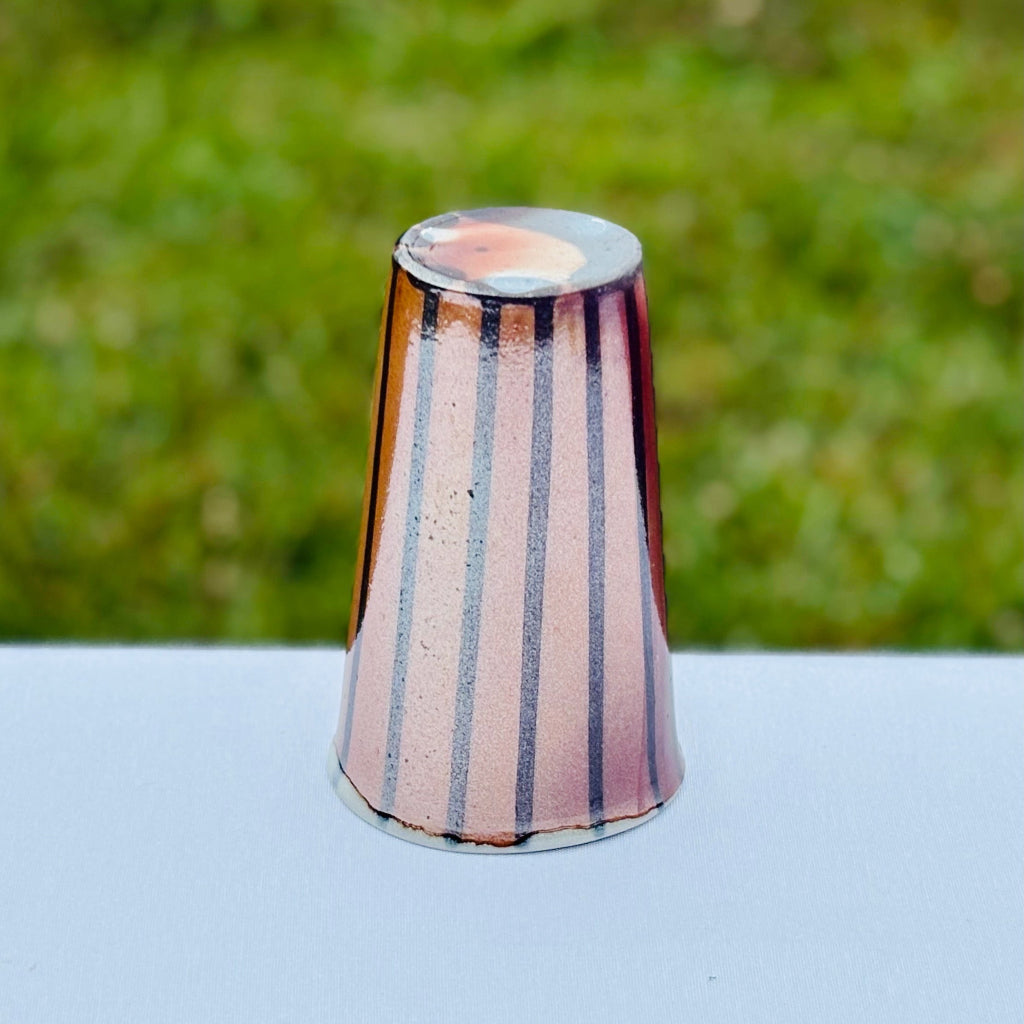 Bottom View: Porcelain tumbler with black drip and artist's mark. Vertical black stripes that contrast with  the soft peach and orange color of the unglazed cup. Made in Danbury, NC. 