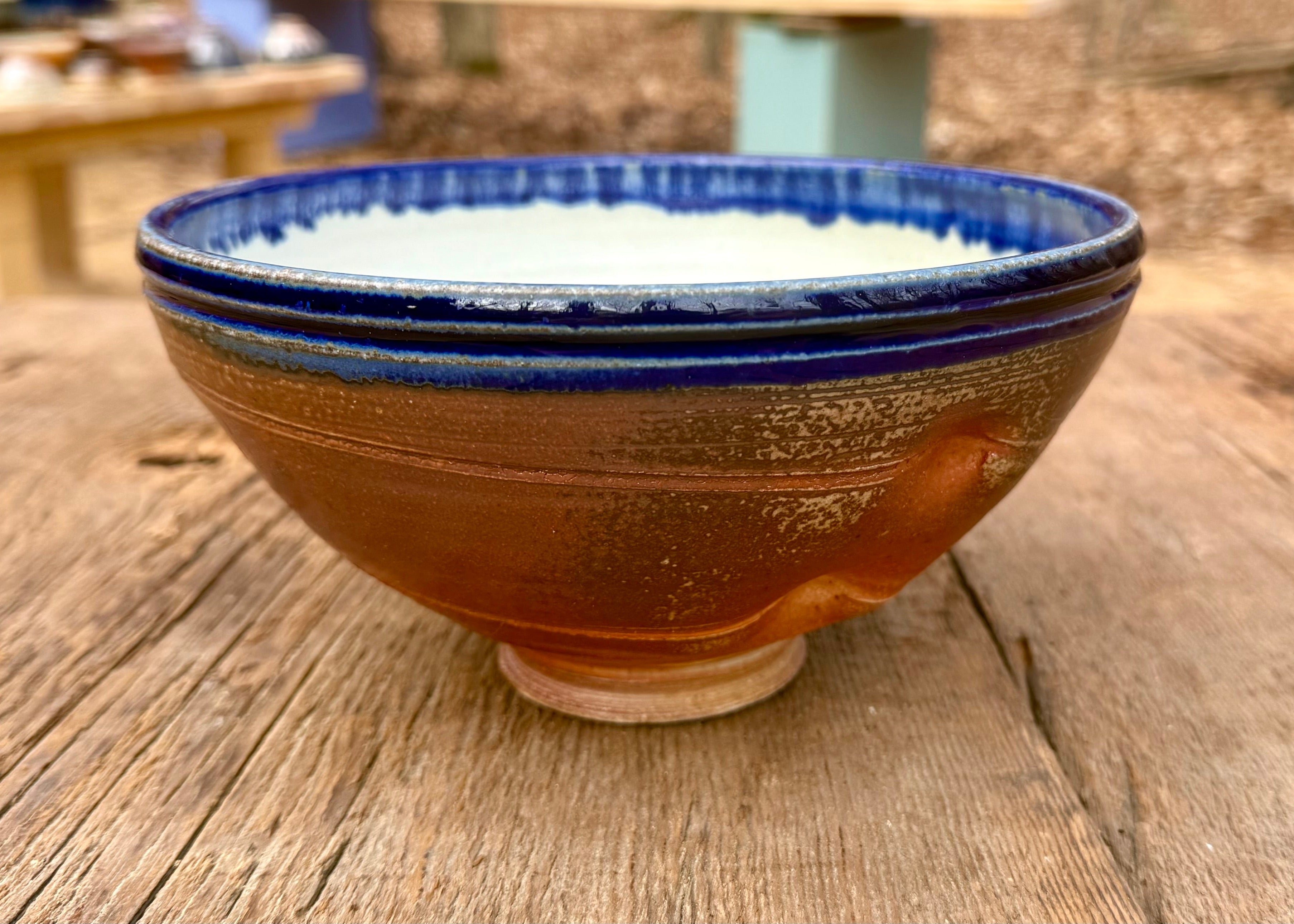Amber brown bowl with a blue rim and white interior accented by diagonal lines and a sturdy base on a wood table.