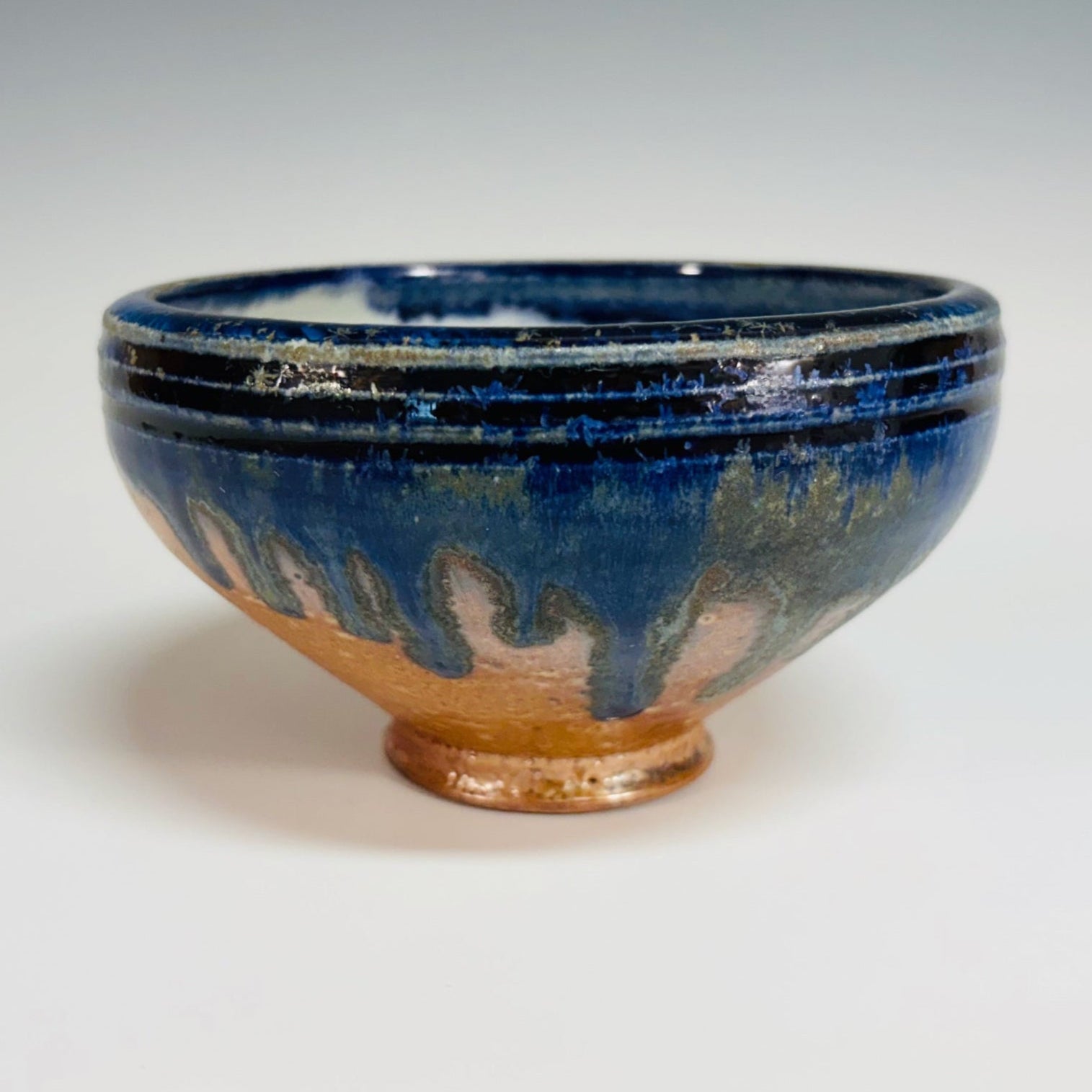 Lovely pottery bowl with a white interior and cobalt drips, three dark blue lines around the rim, and a light brown base.