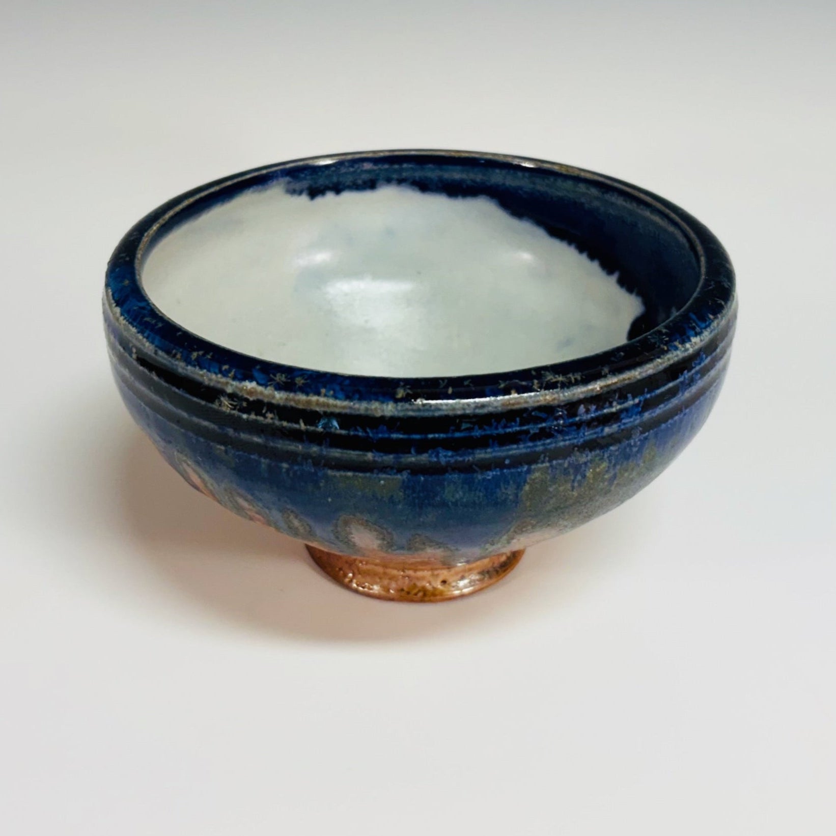 Lovely pottery bowl with a white interior and cobalt drips, three dark blue lines around the rim, and a light brown base.