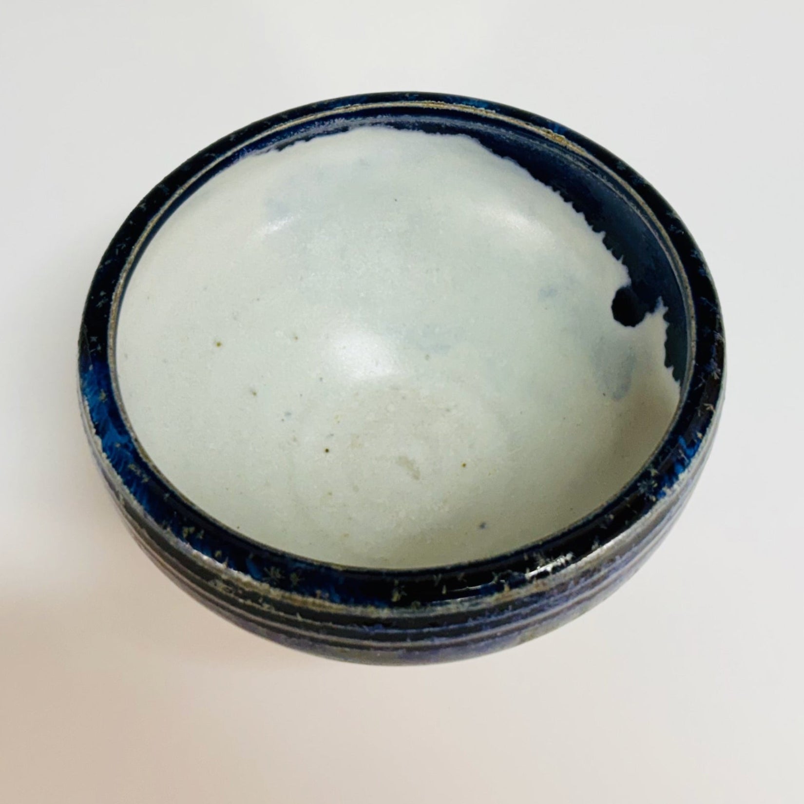 Lovely pottery bowl with a white interior and cobalt drips, three dark blue lines around the rim, and a light brown base.