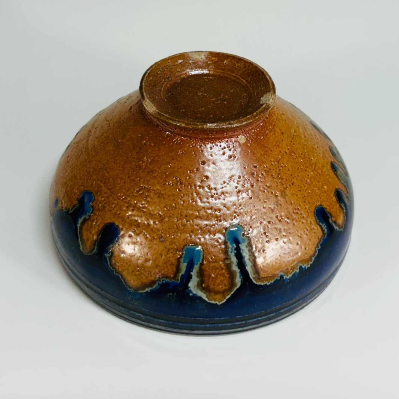 Lovely pottery bowl with a white interior and cobalt drips, three dark blue lines around the rim, and a light brown base.