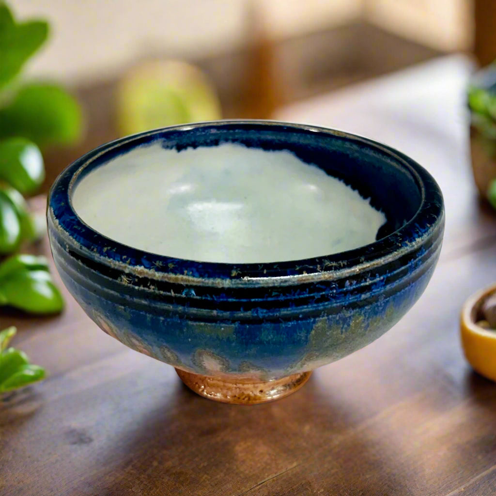 Lovely pottery bowl with a white interior and cobalt drips, three dark blue lines around the rim, and a light brown base.