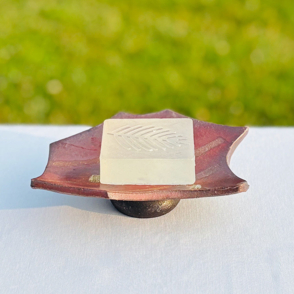Overhead view of handmade pottery soap dish with a bar of soap showing curved design and wood-fired color variations.